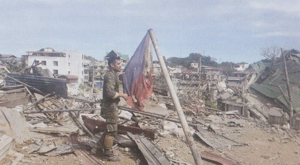 A Marine officer rescues a dilapidated PH flag amid the damaged homes and buildings in Marawi