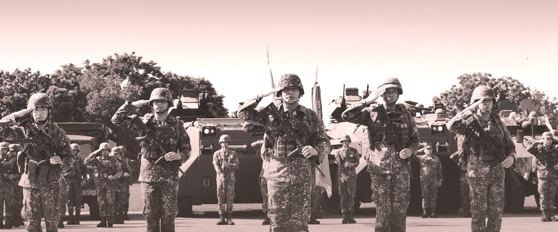 A sepia-toned photograph showing a group of soldiers in uniform saluting. They are adorned with helmets and are carrying rifles. In the background, various military vehicles and equipment can be seen, along with other soldiers standing in formation.